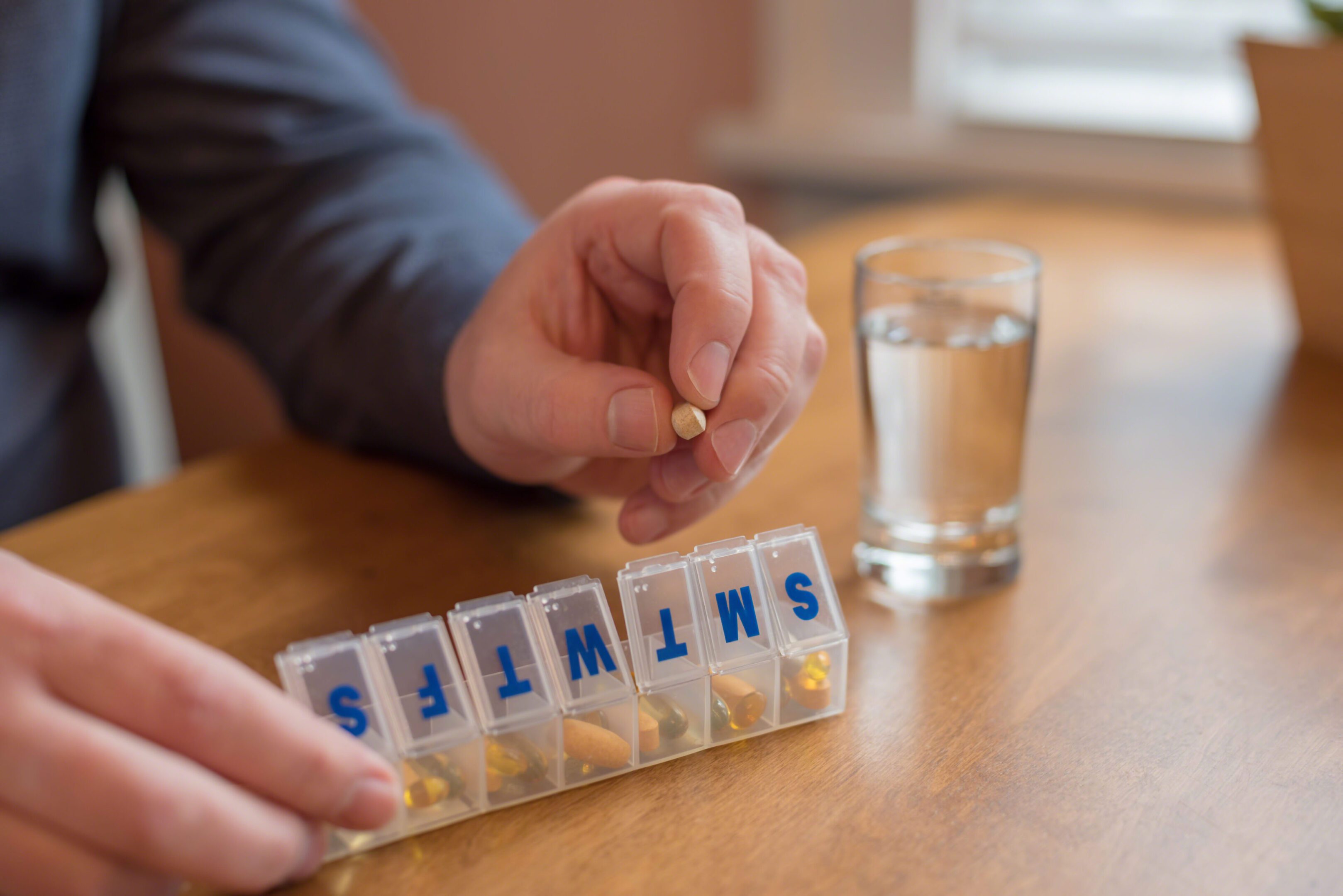 Person organizing pills with water glass nearby.