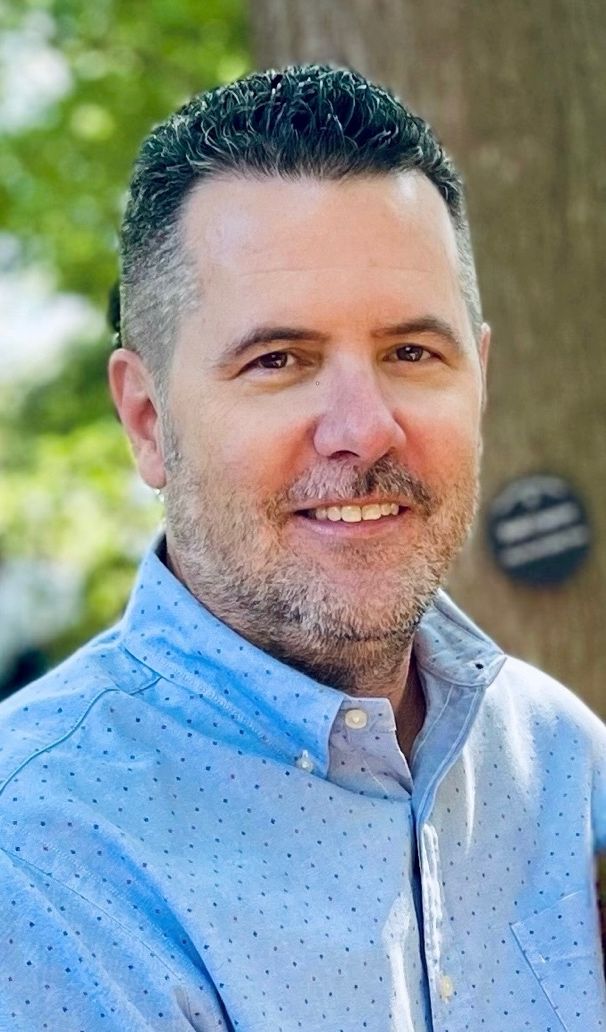 Smiling man outdoors with a tree background.